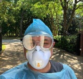 Dr Perry Walton wearing a mask, goggles, scrub cap, and gown with trees behind him.