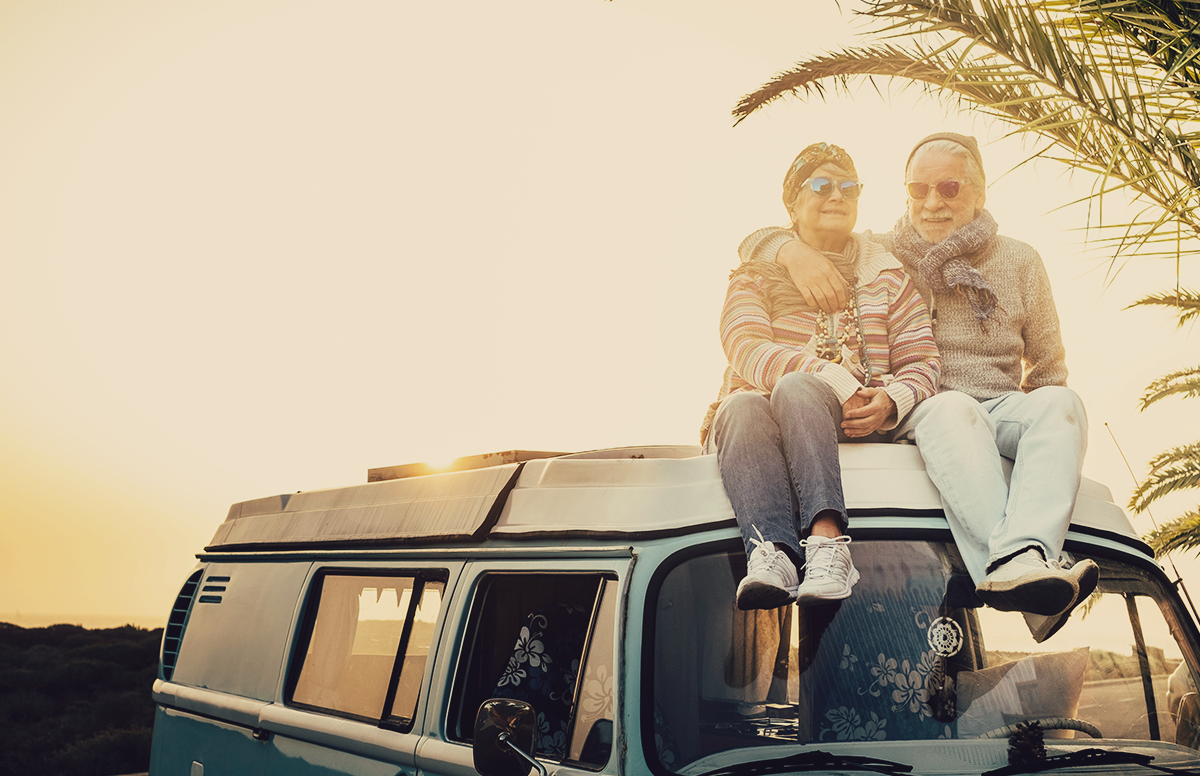 A pair of retired travelers sitting on top of their VW fan, near a beach during sunset