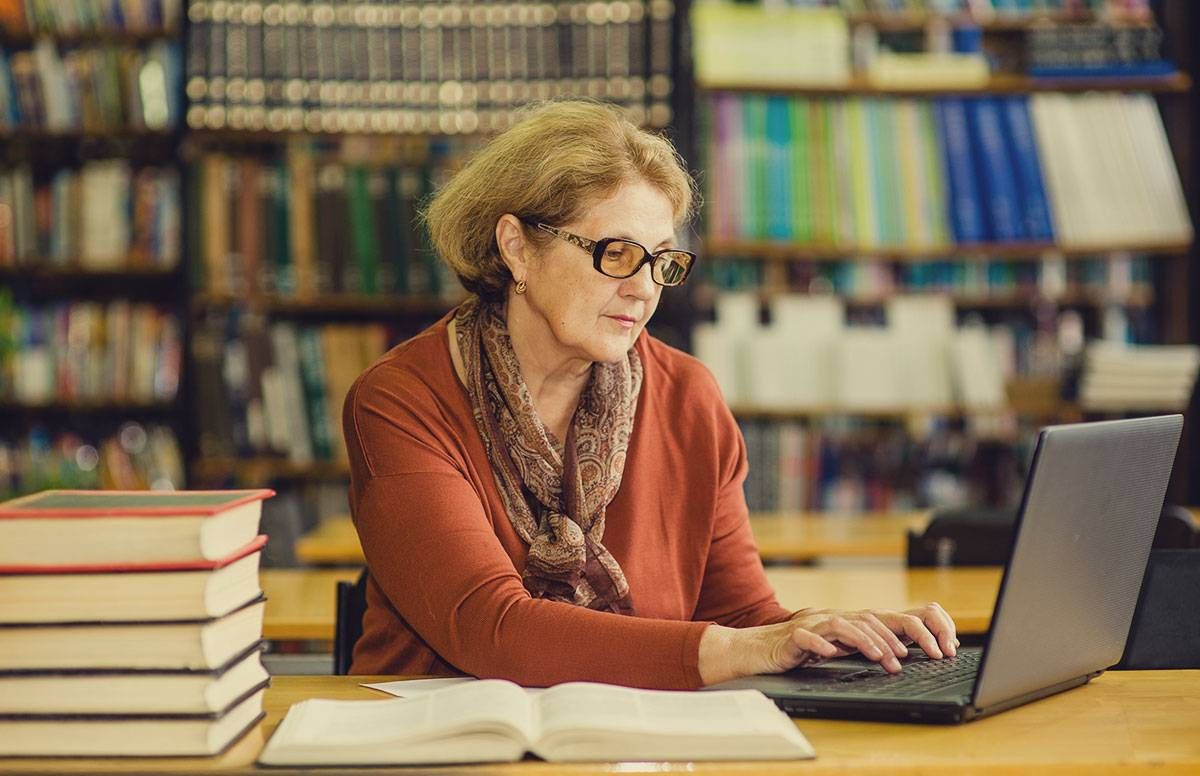 a middle-aged woman in a library, working on a laptop