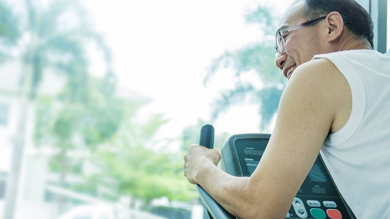 A middle-age man on an exercise machine, looking out a window with palm trees in the distance