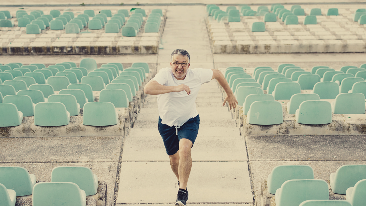 a middle-age man running up a series of stairs in an empty stadium