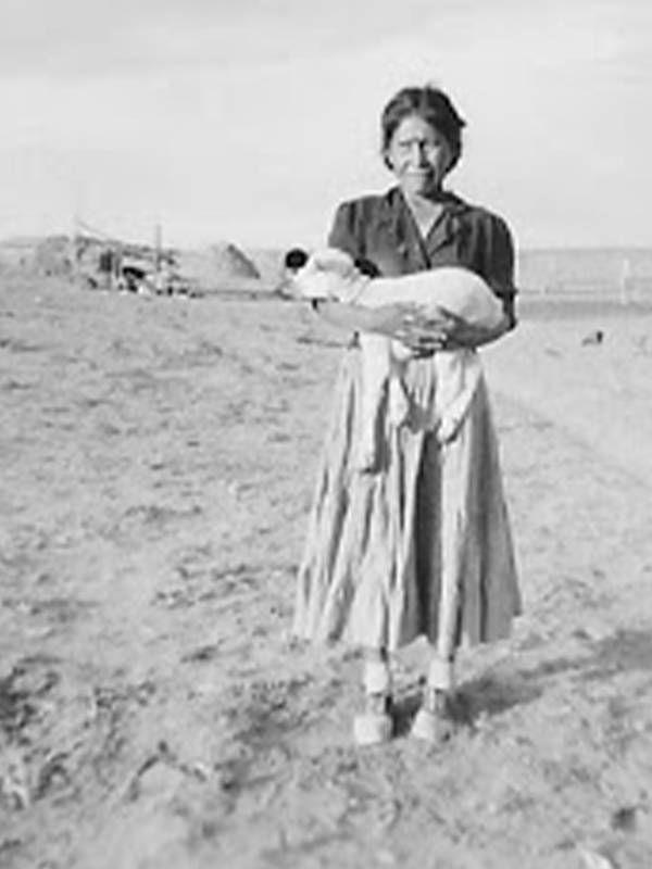 Old photograph of a Navajo Woman standing outsider her home holding a baby lamb, tribal elders, COVID-19, Next Avenue