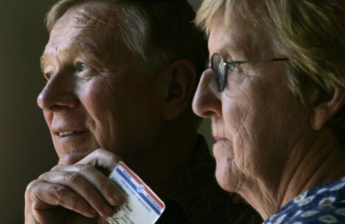 Older couple looking out window holding a Medicare card