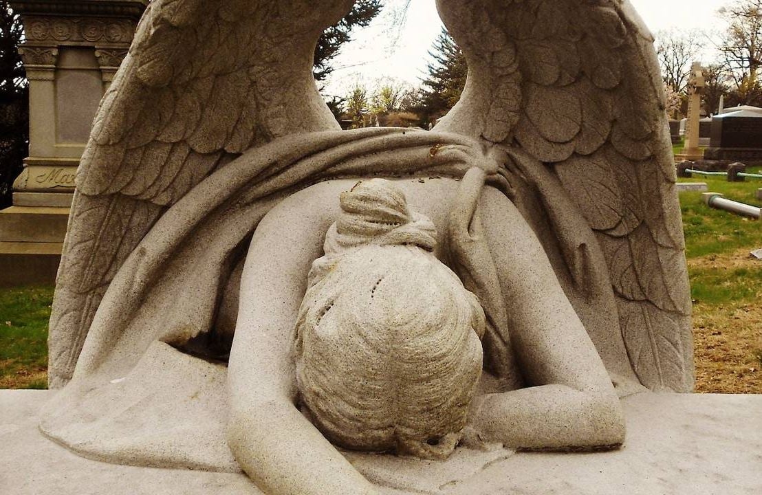 An angel statue laying her head down at a cemetery, grief, funerals, Next Avenue