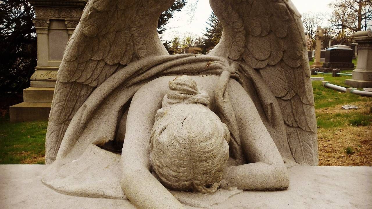 An angel statue laying her head down at a cemetery, grief, funerals, Next Avenue