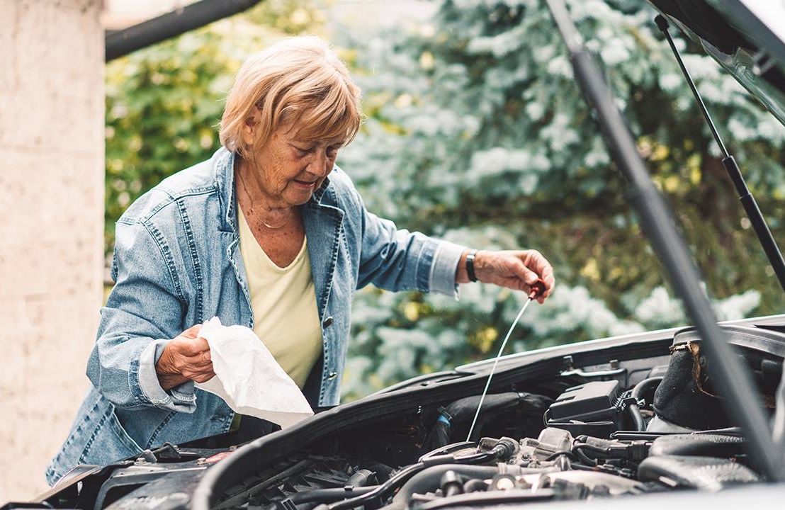 Middle aged woman checking the oil under the hood of her car, car maintenance , Next Avenue