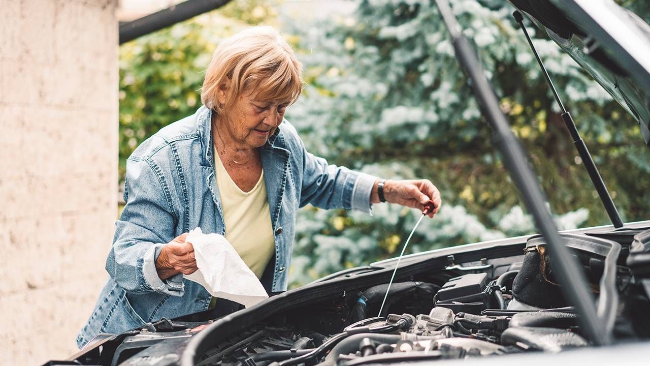 Middle aged woman checking the oil under the hood of her car, car maintenance , Next Avenue