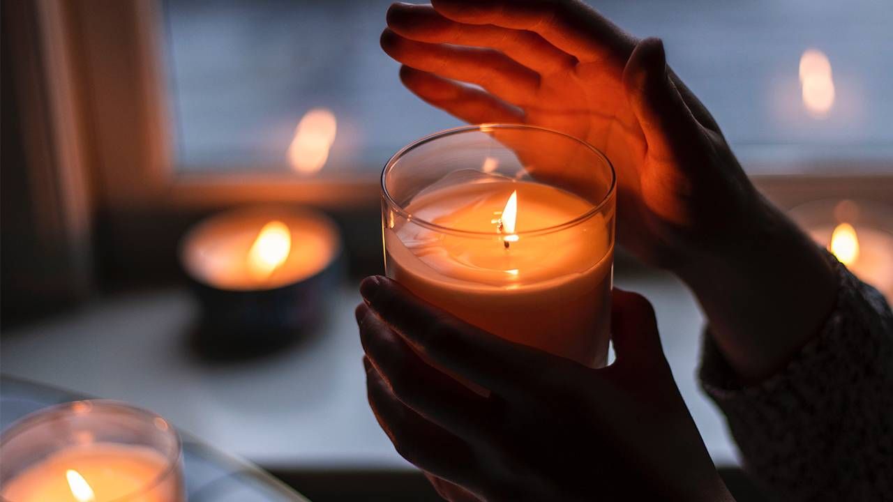 A person holding a lit candle at home funeral, Next Avenue