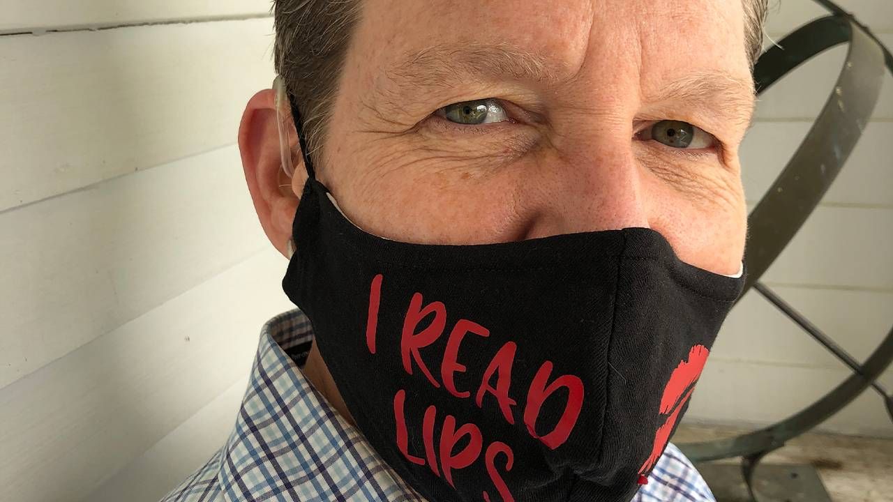 Close up of a middle aged woman wearing hearing aids and a face mask that says, "I read lips", lip readers, Next Avenue