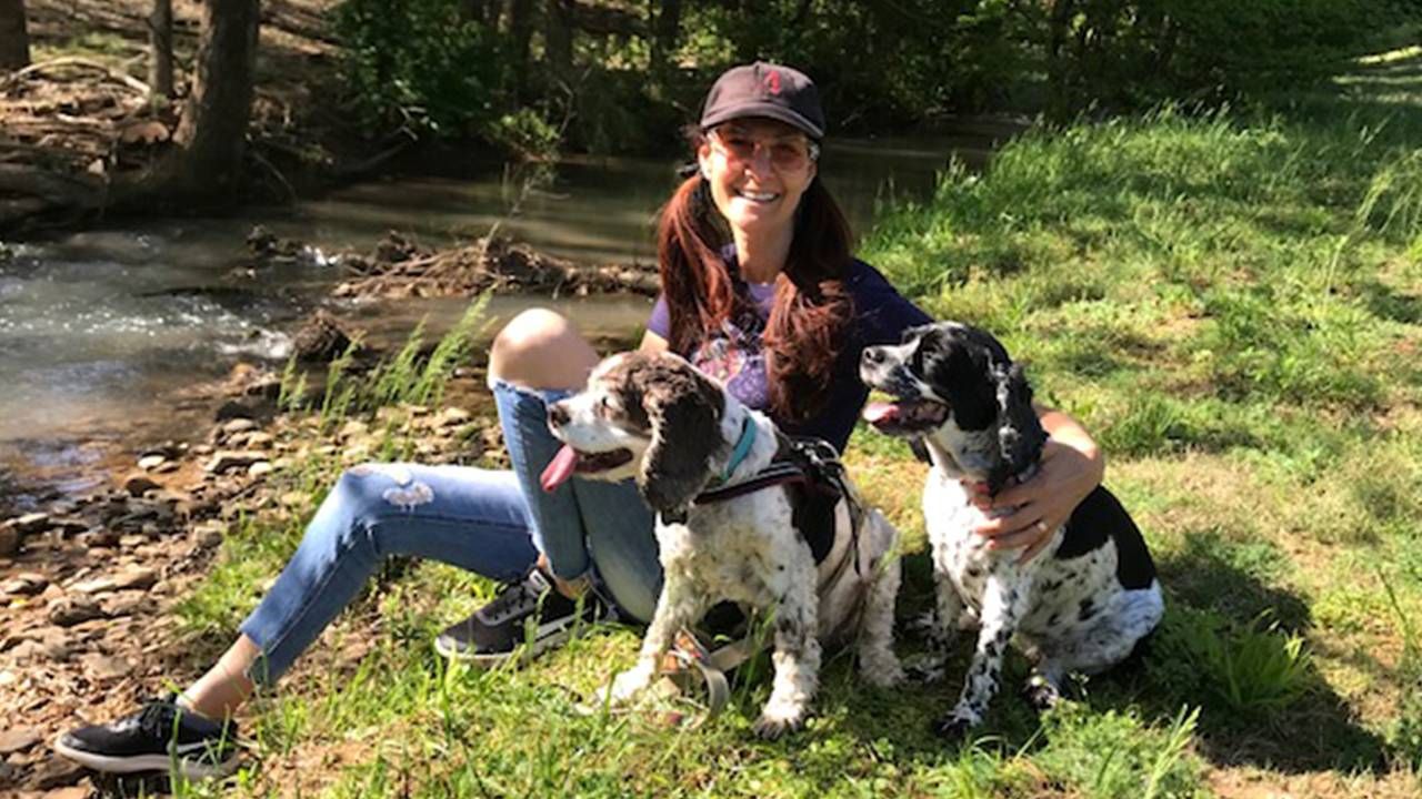 woman sitting by a stream with her two dogs, pet dementia, CDS, Next Avenue