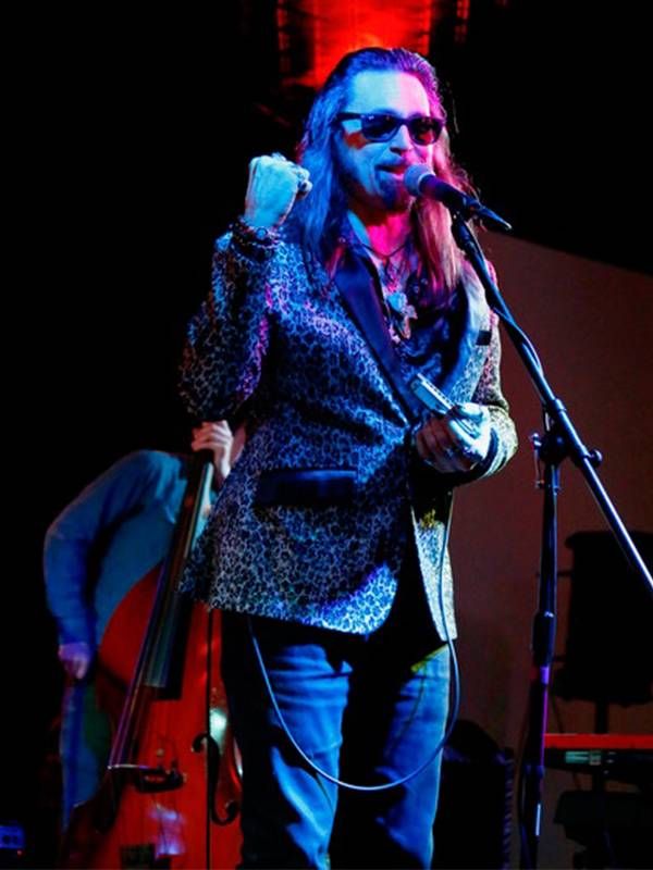 Man wearing a leopard print blazer playing harmonica live on stage, Next Avenue