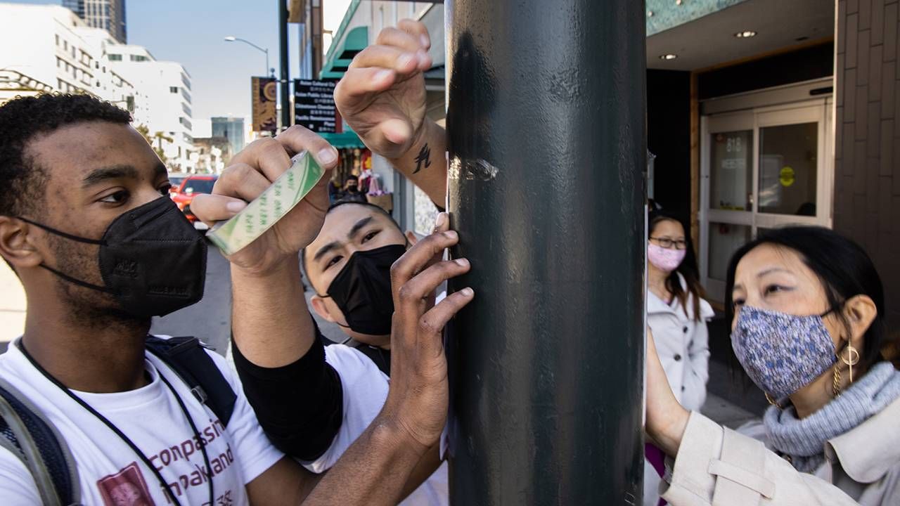 Three young people tape poster to light pole, hate crimes, activism, Next Avenue