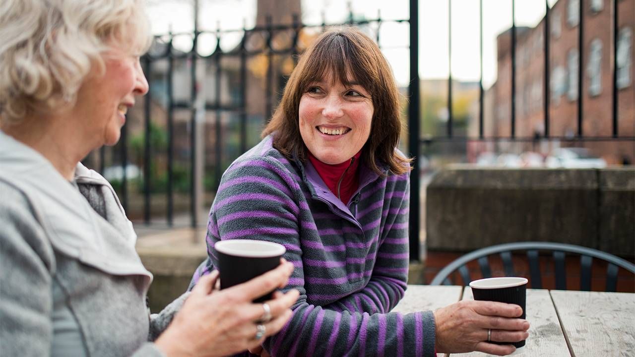 An older woman and a younger woman sitting and talking drinking coffee. 12-step programs, loneliness, Next Avenue