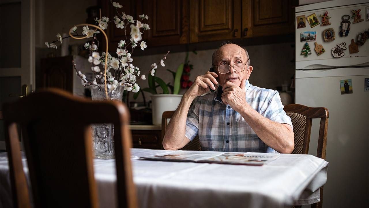 Older adult man talking on the phone sitting at the kitchen table. Medical, hospital, Next Avenue