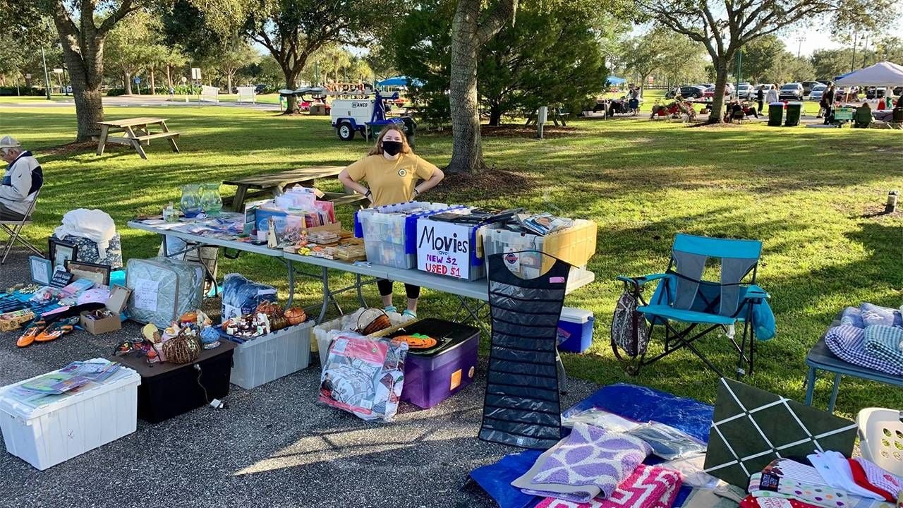 An outdoor yard sale with a young adult standing behind a table full of items. Next Avenue