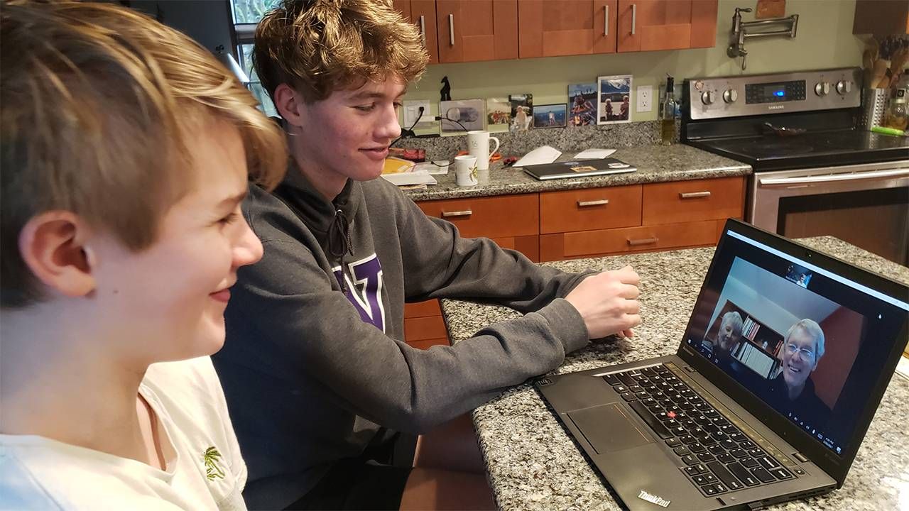 Two young boys in a kitchen Zooming with their grandpa.