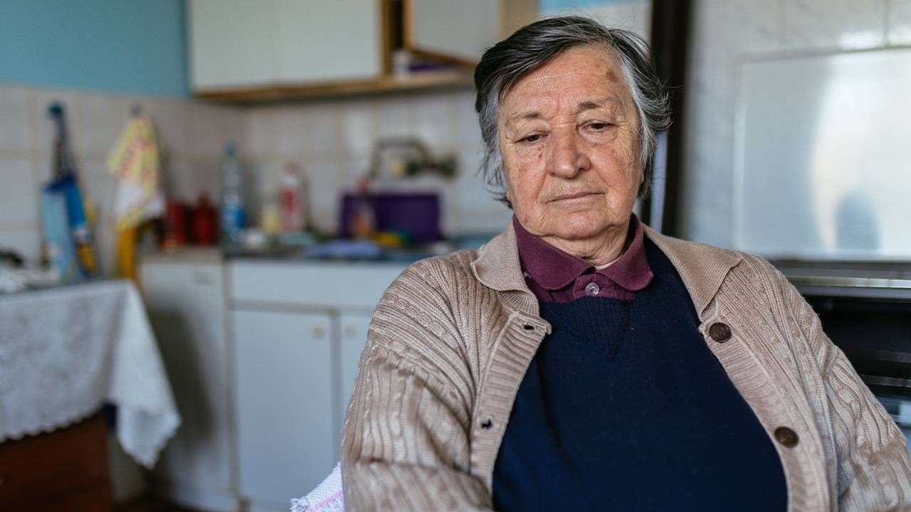 Older woman sitting in kitchen looking down. Self-neglect, elder abuse, Next Avenue