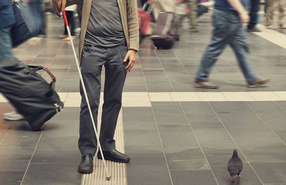 A blind man walking through an intersection using a walking stick.
