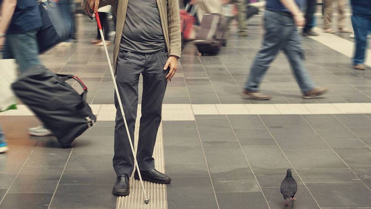 A blind man walking through an intersection using a walking stick.