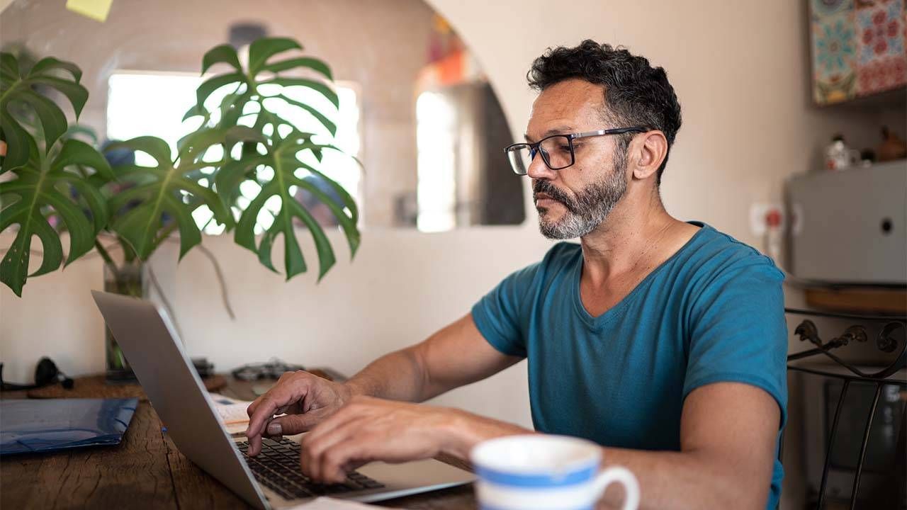 An older man with a greying beard looking for a job on his laptop at home. New job, onboarding, Next Avenue