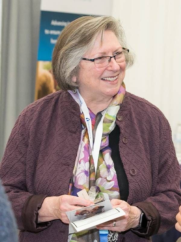 A woman standing at a conference smiling and holding brochures. Diversity, equity, inclusion, Next Avenue