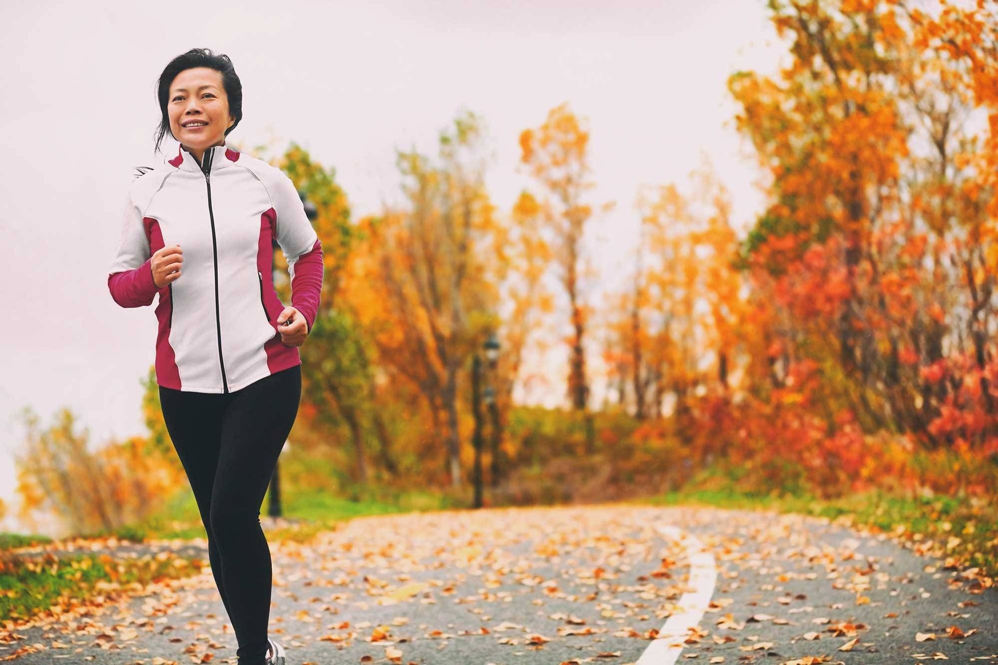 A woman runs on a running path with trees in fall colors behind her.