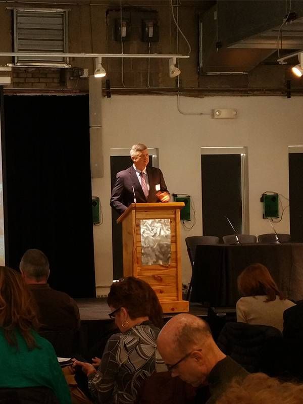 An older man standing a podium at a conference. Age diversity, ageism, work, Next Avenue