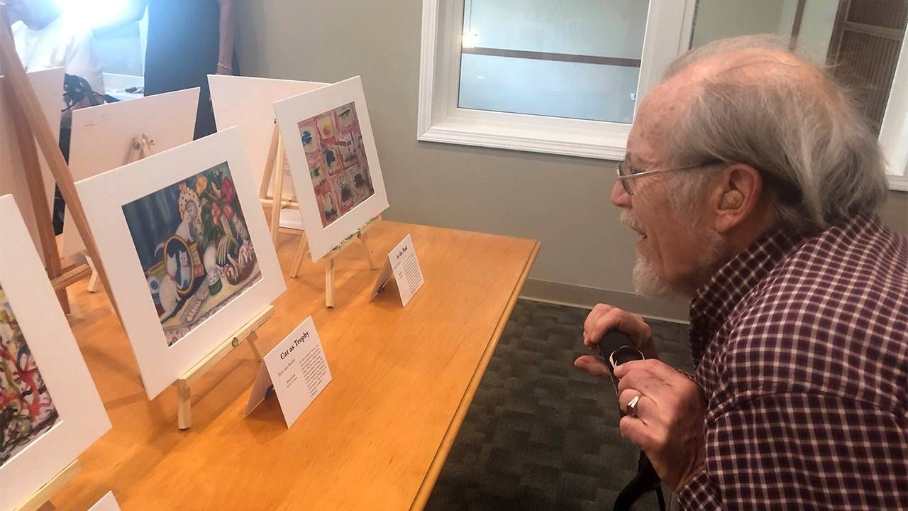 An older adult looks at a set of paintings in an art exhibit. Community, dementia, Next Avenue