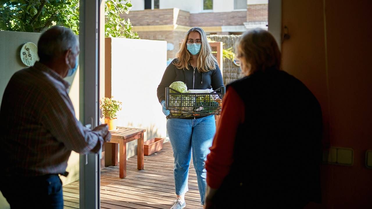 A young adult delivering groceries to an older couple at home. aging-service, aging services, Next Avenue