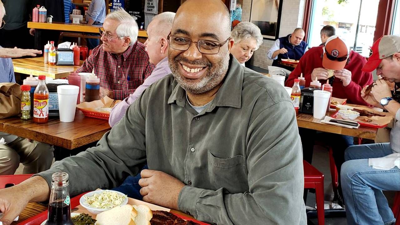 Author Adrian Miller at a BBQ restaurant smiling. barbecue, African American Black cooks, Next Avenue