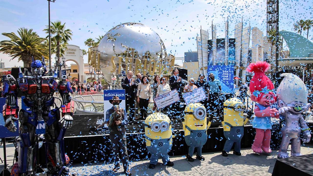 Confetti and costumed characters surround CA governor. Vaccine incentives, COVID-19, Next Avenue