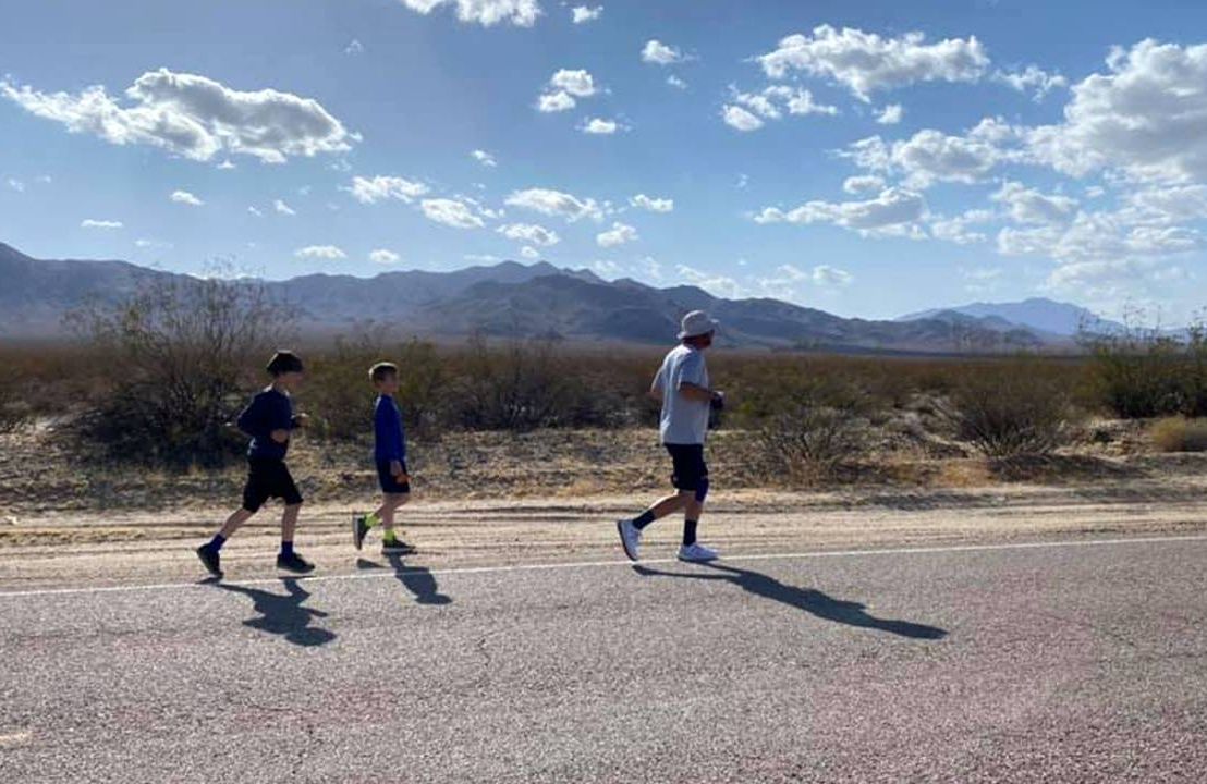 A man running on a desert road with kids behind. Next Avenue