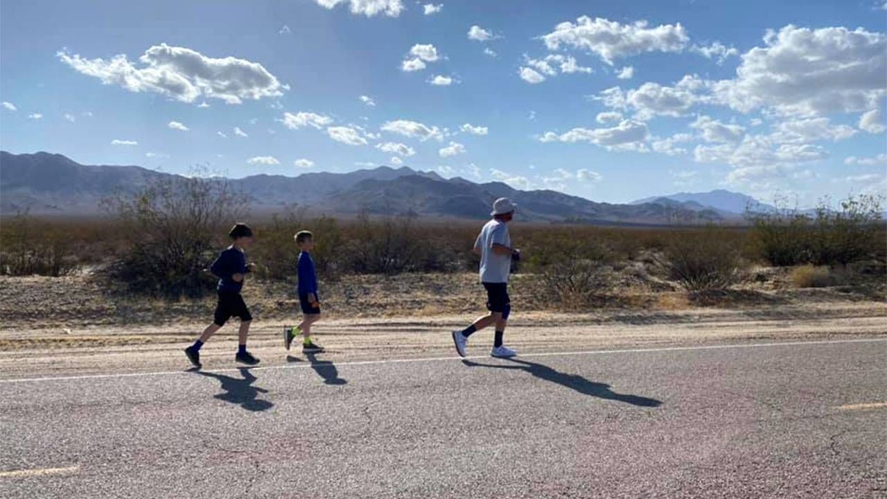 A man running on a desert road with kids behind. Next Avenue