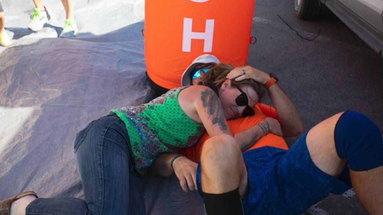 A man hugging his wife laying down at the finish line. Running, Next Avenue