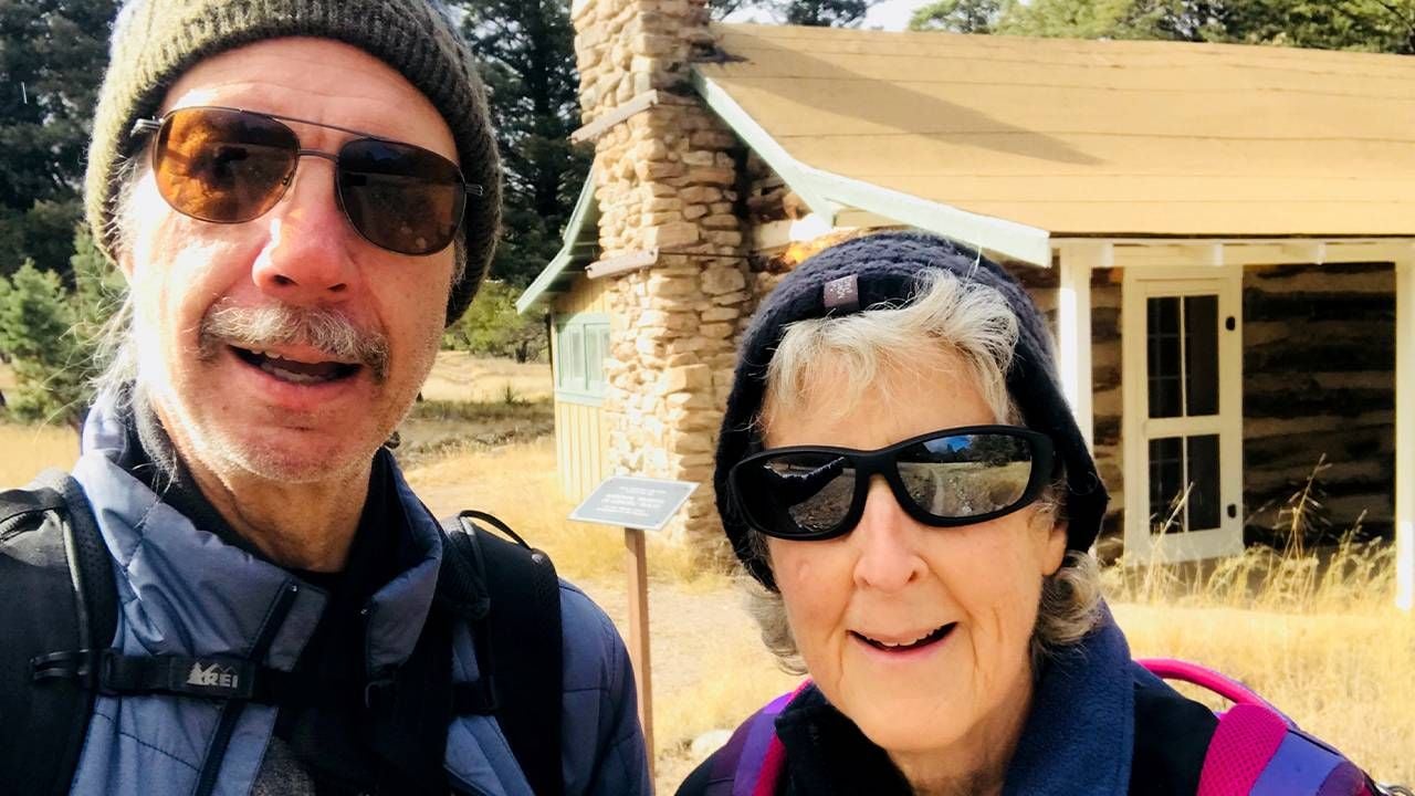 An older couple smiling in front of a log cabin. Retirement, rural, Next Avenue, health care