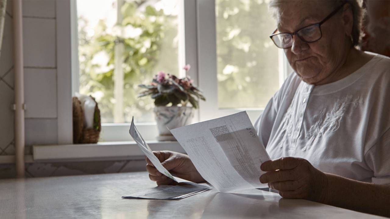 An older woman sitting at her table, looking at her bills. Next Avenue, senior poverty