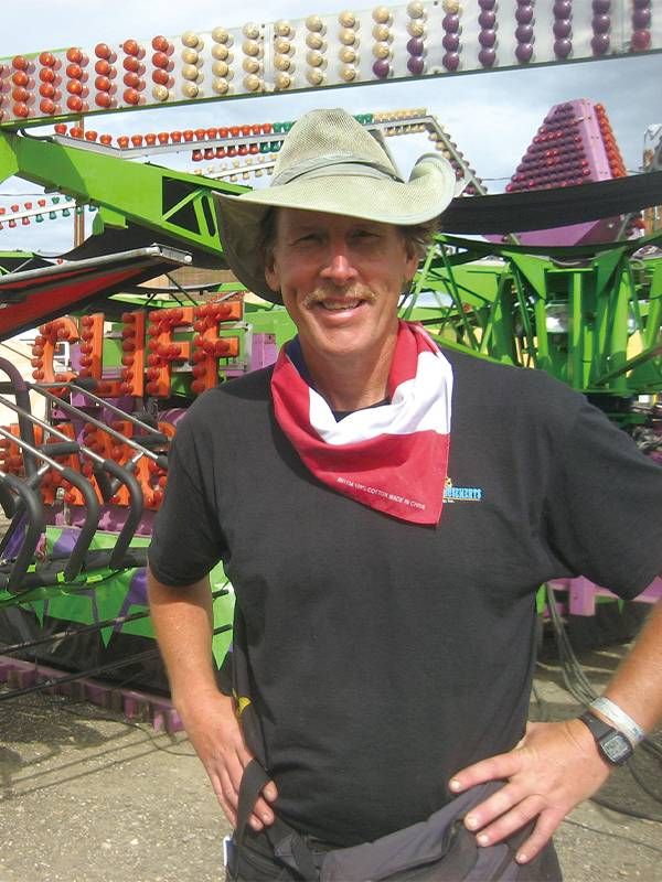 Michael Sean Comerford standing in front of a cliff hanger carnival ride. Next Avenue route 66, carnival