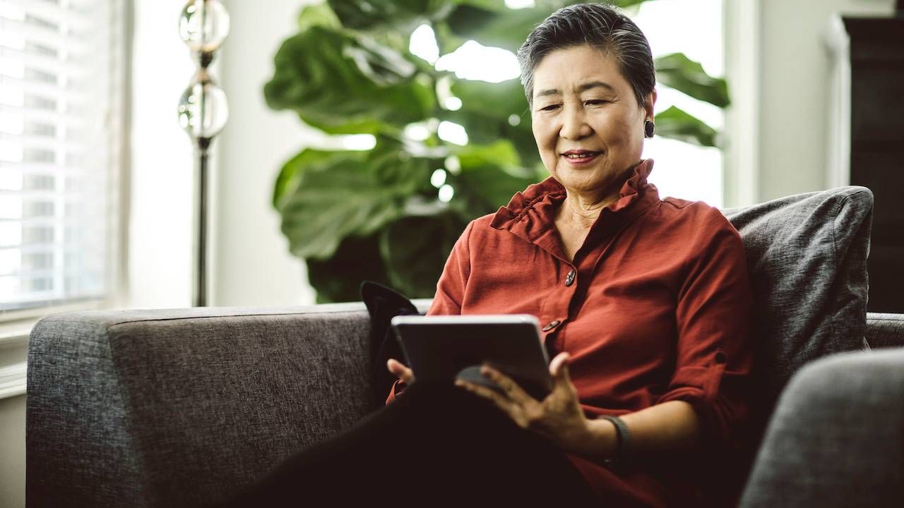 A photo of a person sitting on their couch reading a tablet computer.