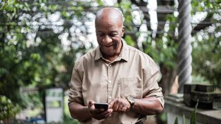 A man outdoors, smiling while looking at his phone. Next Avenue, solo aging, connecting, friends