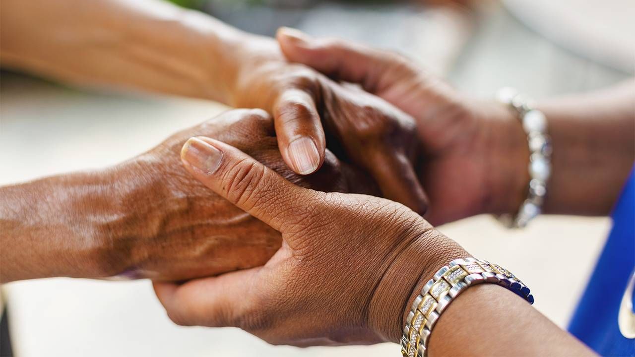 An adult caregiver holding her mother's hands. Next Avenue, paid family leave, family caregiving