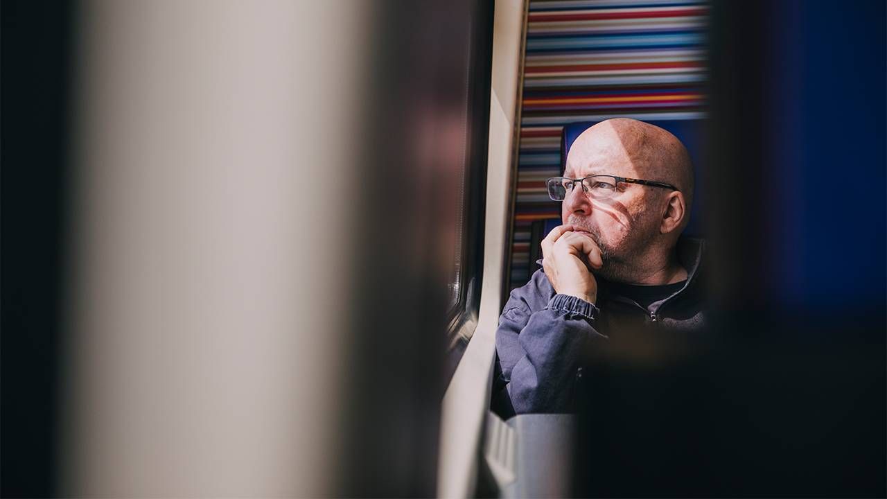 A man sitting alone looking out a train window. Next Avenue, diagnosis