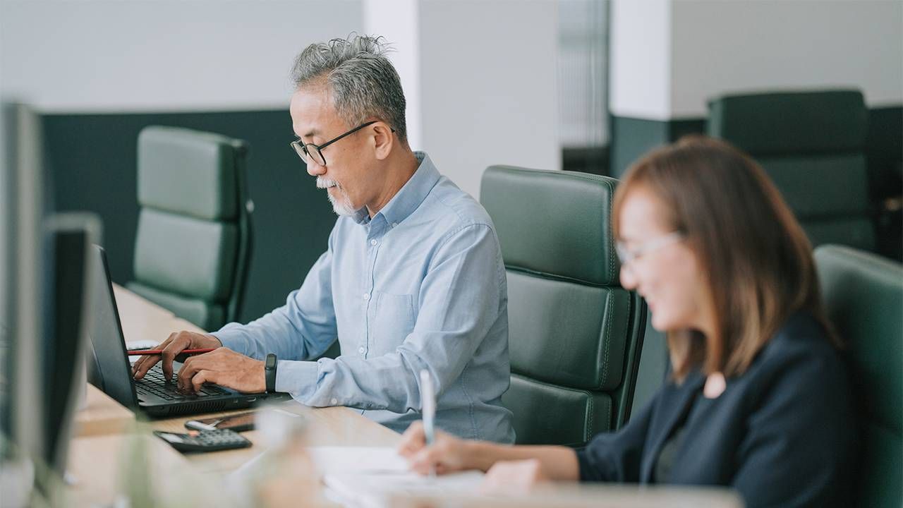 Two older people smiling while working at the office. Next Avenue, age-friendly jobs, workplace, age-friendly institute