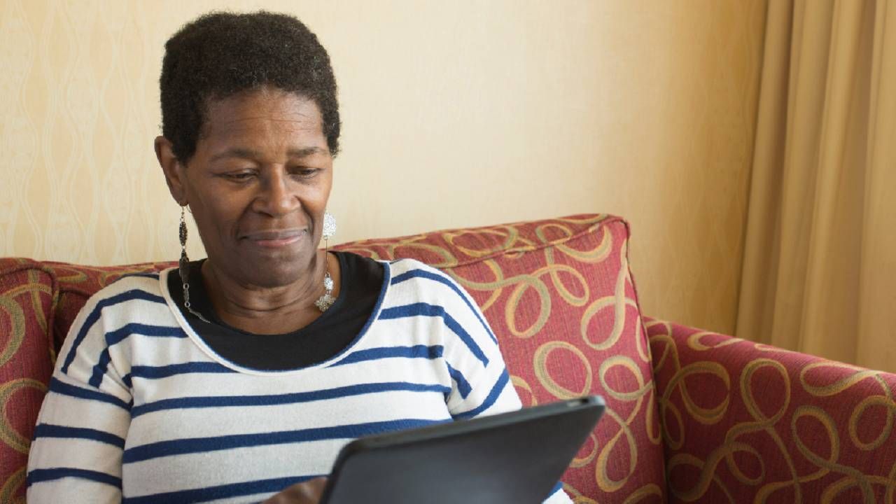 Older person sitting on a couch researching something on their tablet.