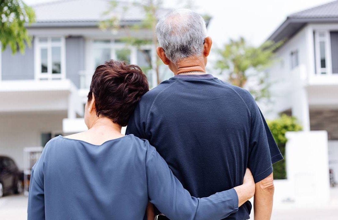 A couple standing in front of a new house. Next Avenue, relocating in retirement, where to live in retirement