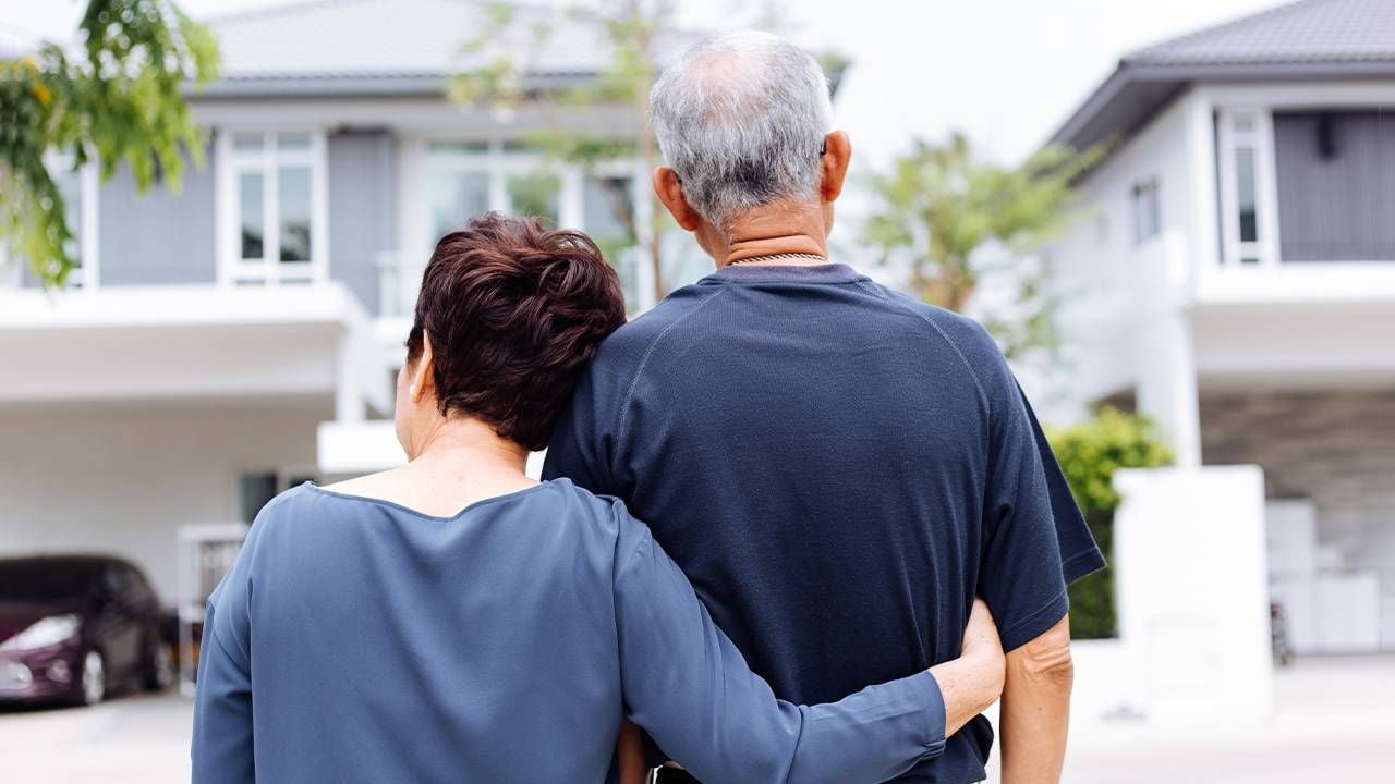 A couple standing in front of a new house. Next Avenue, relocating in retirement, where to live in retirement