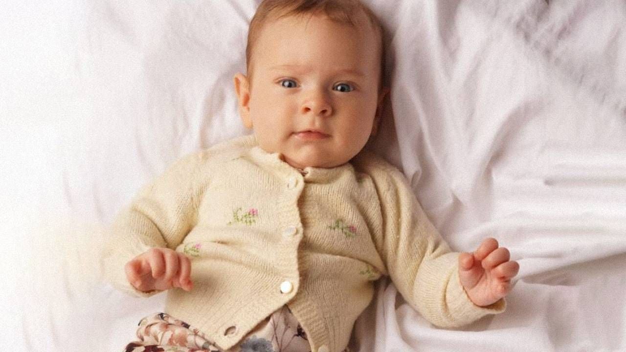 A baby wearing a knitted sweater laying on a white sheet. Next Avenue, family heirloom, sweater