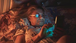 A woman laying in bed looking uncomfortable on her phone. Next Avenue, symptoms of perimenopause, what is perimenopause