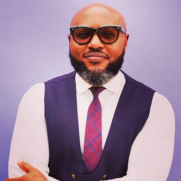 Headshot of a man wearing sunglasses and a checked tie. a Next Avenue