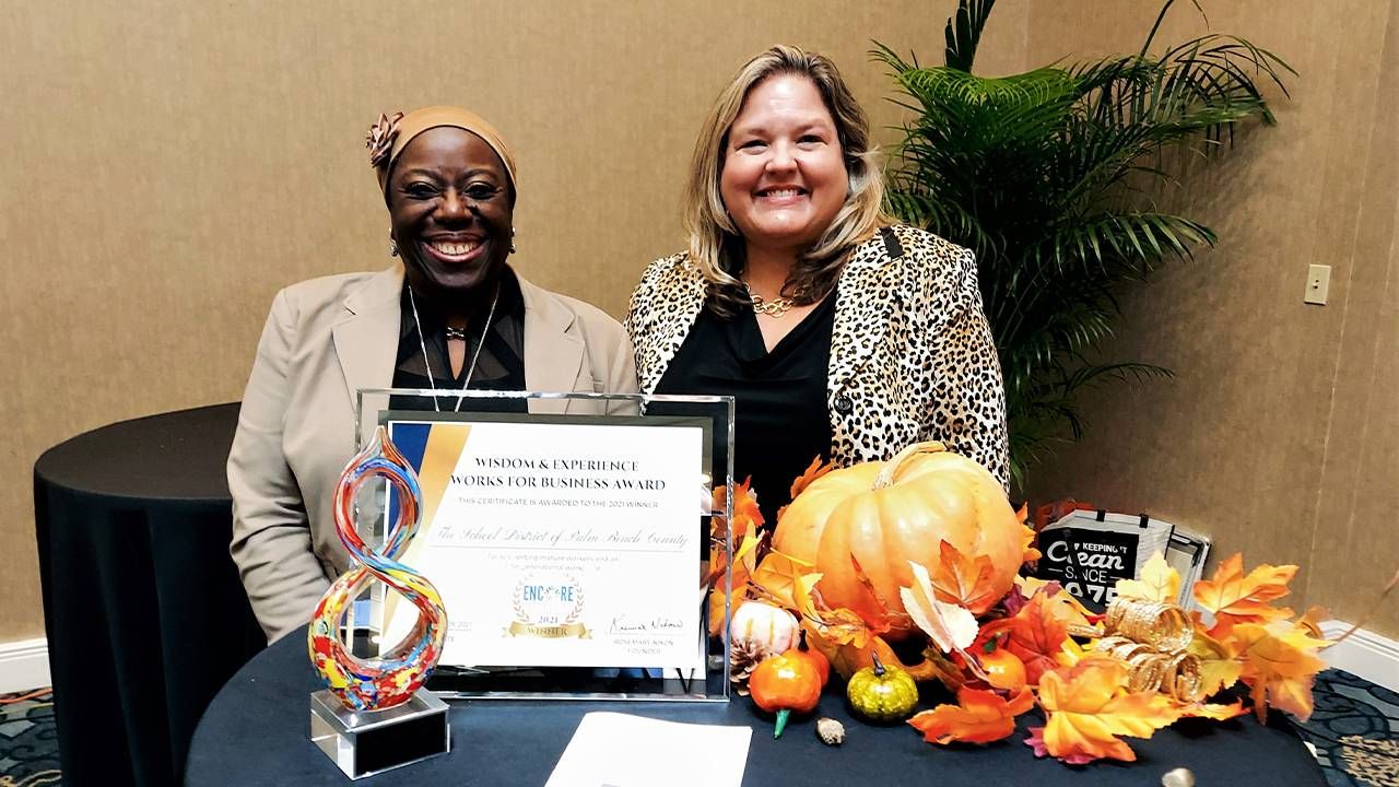 Two women ssitting at a table in front of two awards, smiling. Next Avenue, older workers, reckoning