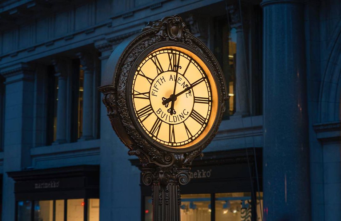 A old fashioned clock on the street in New York, glowing at night during daylight savings time. Next Avenue